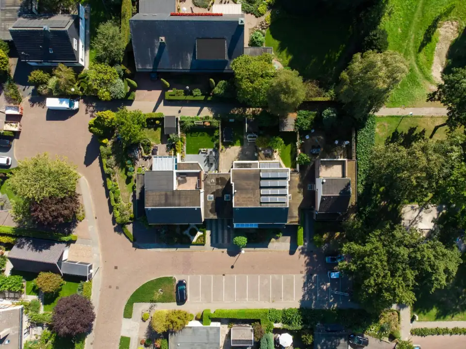 Een woonwijk van bovenaf, met zonnepanelen op enkele platte daken en tuinen ertussen