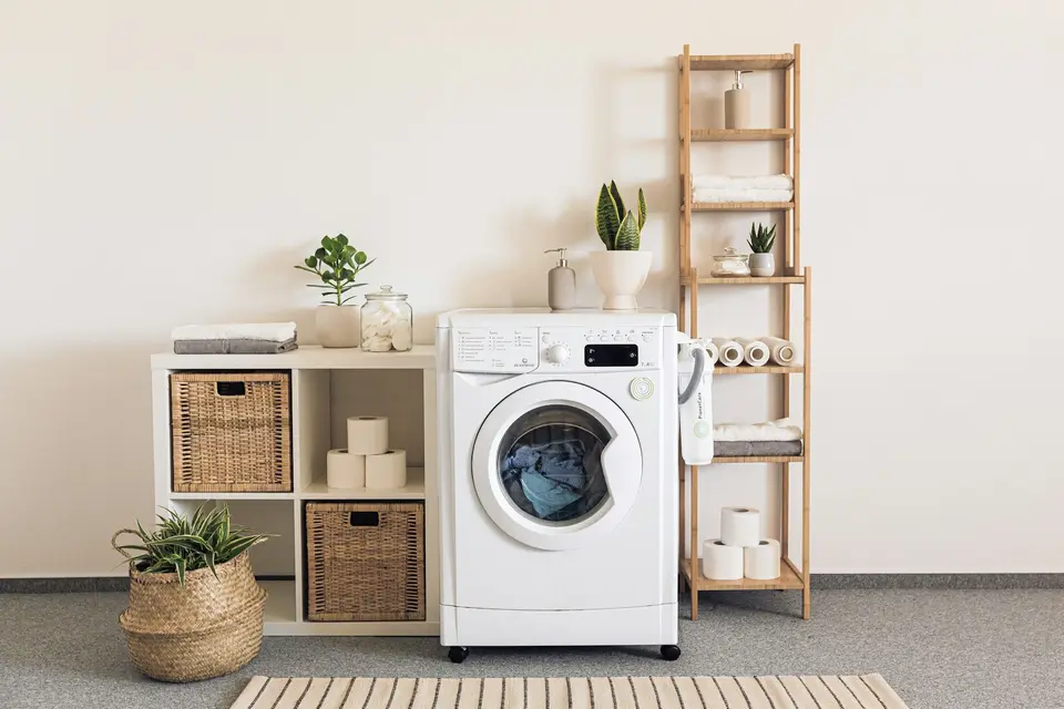 Een wasmachine met was in de trommel in een lichte bijkeuken, met rekken en manden