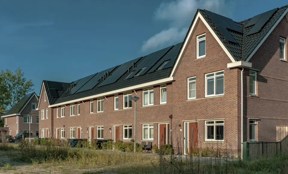 Een rij nieuwe rijtjeshuizen van rode baksteen met zonnepanelen over het hele dak, in laag middaglicht