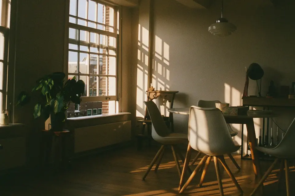 Een eetkamer in een Amsterdams bovenhuis, met laag zonlicht door een hoog raam op de houten vloer